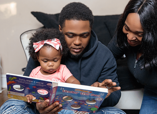 A family of 3 sitting reading a book