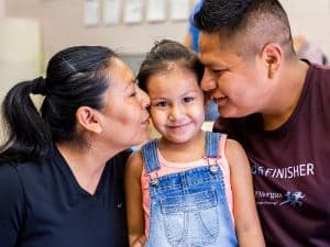 Mother and father kissing child on cheek