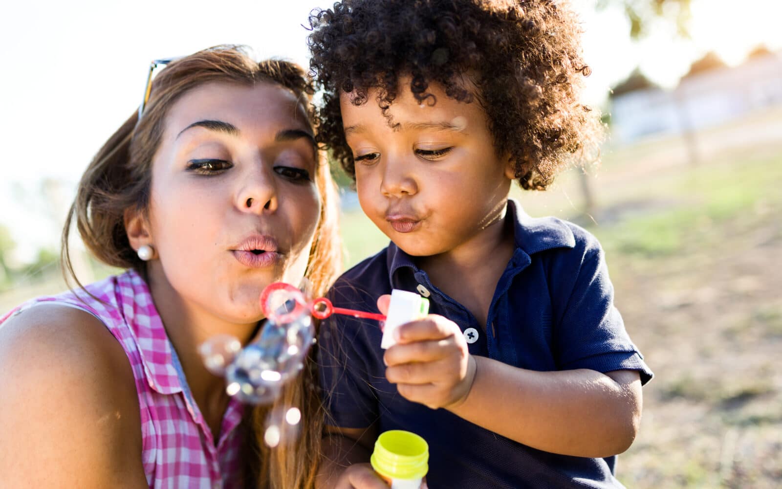 Portrait of beautiful young mother with her son blowing bubbles in the park.