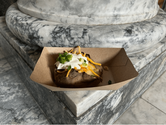 Photo of a baked potato with "all the fixings" on the ledge of a marbled stone pillar in Olympia, WA in February 2025 for Potato Day.